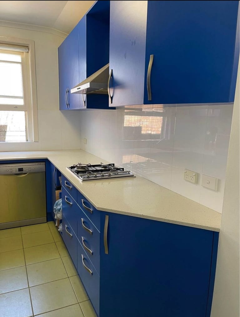 Modern kitchen with blue and white cabinetry, white countertop, gas cooktop, and glass backsplash