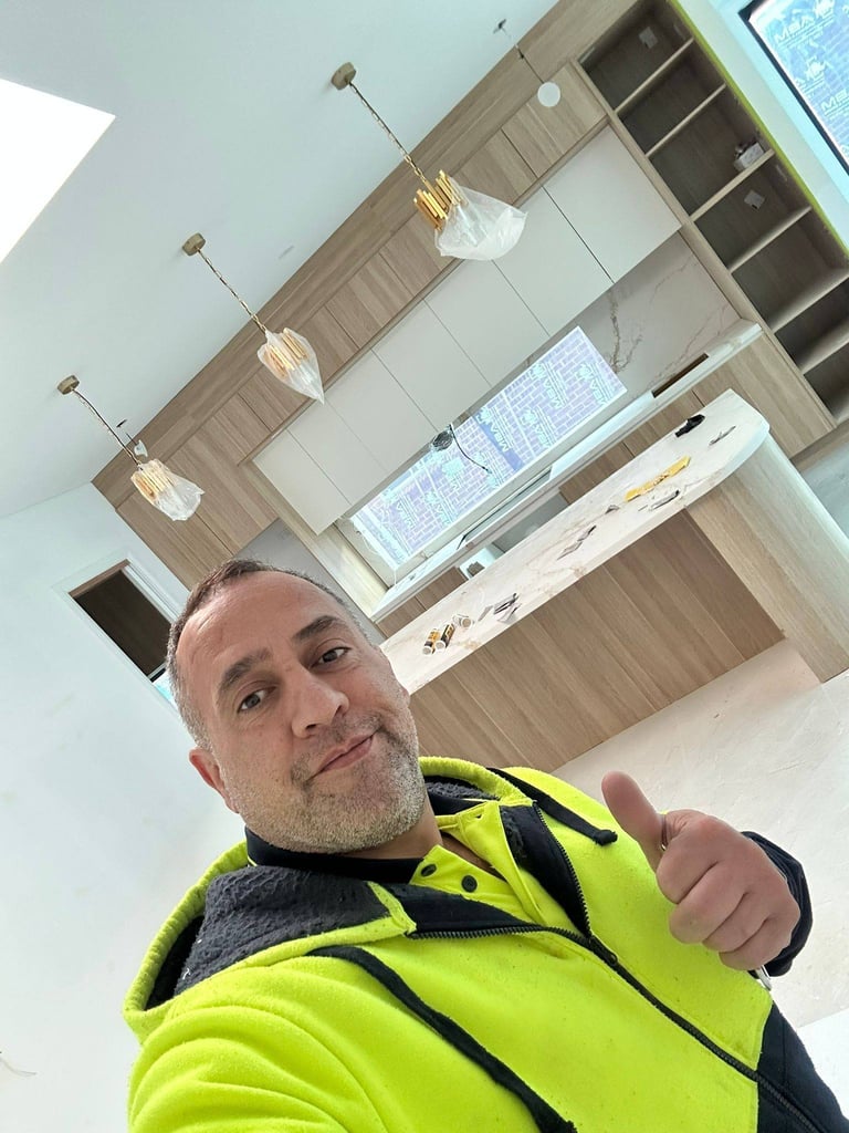 Man in neon yellow jacket taking selfie in modern kitchen with pendant lights and wooden cabinetry