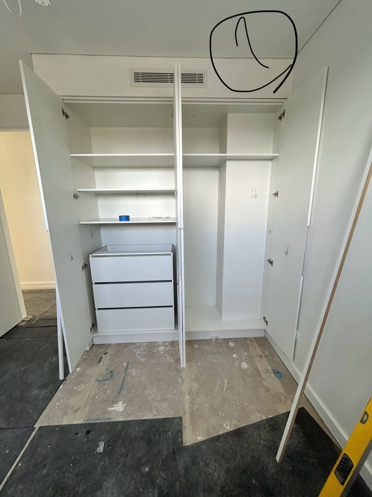 Empty closet interior with white shelving, white dresser drawers on left side, and concrete floor during renovation