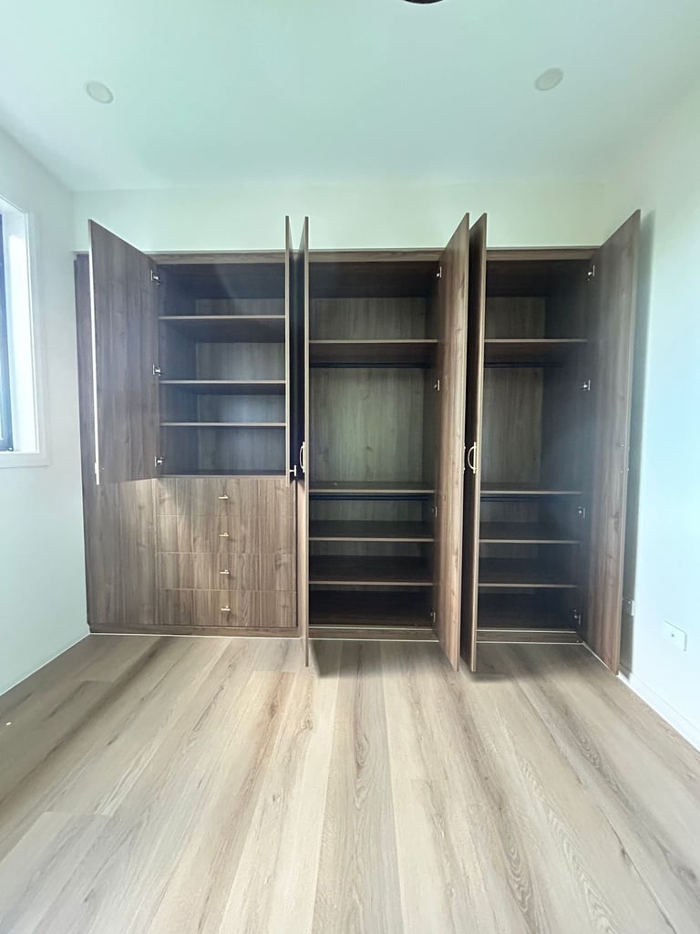 Built-in wardrobe with dark wood finish and open doors revealing shelves and hanging space in empty bedroom