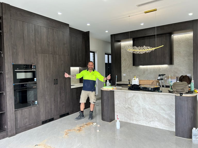Construction worker in neon safety vest standing in modern kitchen under renovation with dark cabinets and marble countertop