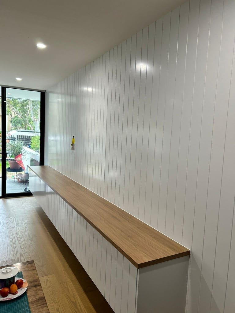 Modern interior with long wooden countertop against white vertical wall paneling and glass door leading outside