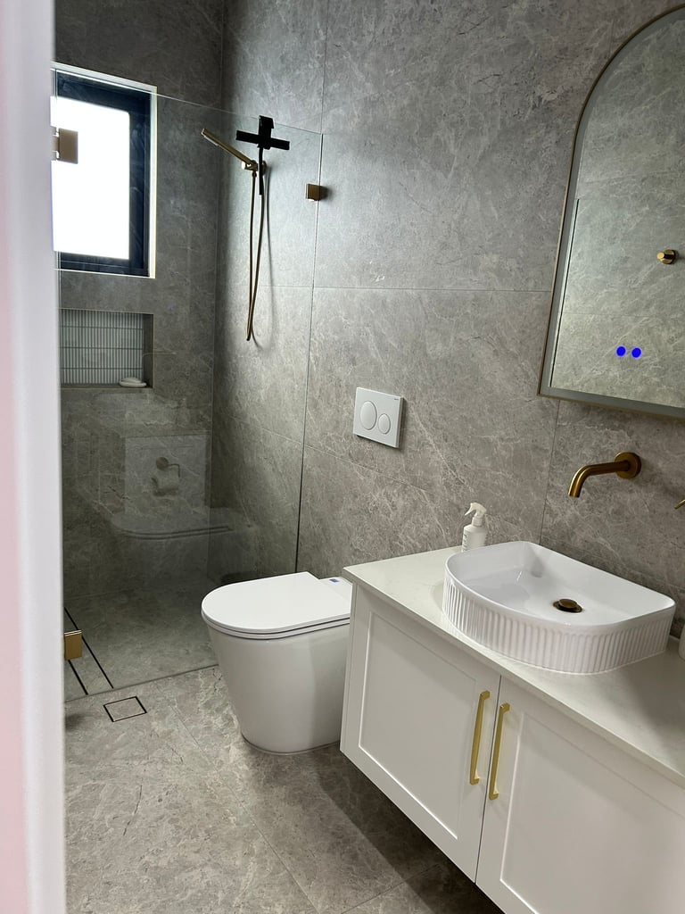 Modern bathroom with gray tile walls, white vanity sink, toilet, and walk-in shower with glass partition