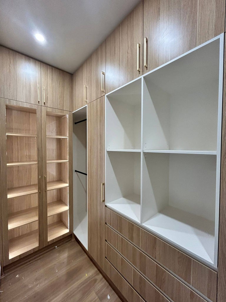 Modern walk-in closet with wood-grain cabinetry, glass-door wardrobe on left, and white shelving unit on right with recessed lighting
