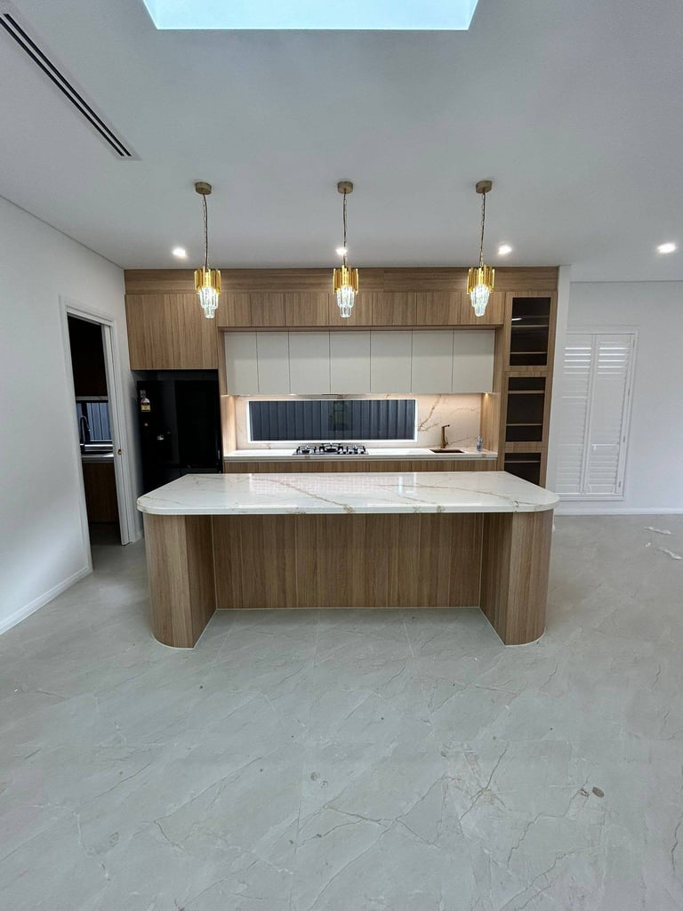 Modern kitchen with wooden curved island, white countertops, pendant lights, and built-in appliances under skylight