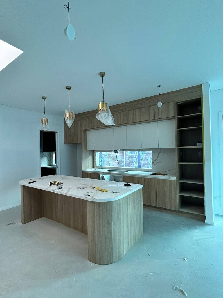Modern kitchen interior with wood and white cabinetry, island counter, pendant lights, and open shelving under construction.