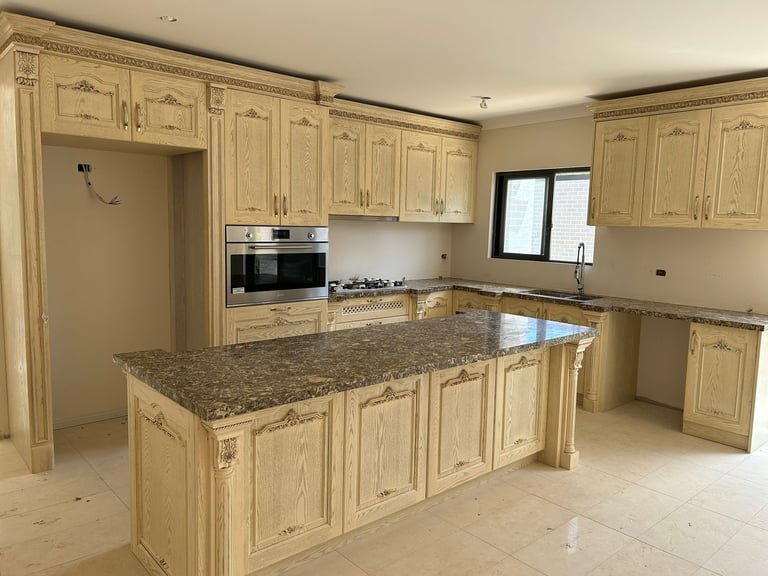 Modern kitchen with cream-colored wooden cabinets, granite countertop island, built-in oven, and stainless steel appliances