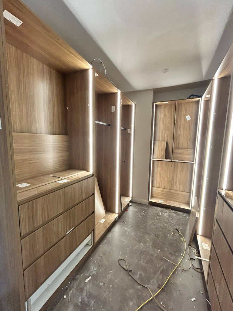 Modern bathroom under construction with wooden cabinetry, LED lighting, and glass shower enclosure