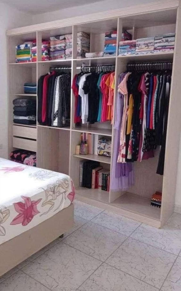 Organized bedroom closet with white shelving units containing folded clothes, hanging garments on rails, and storage compartments