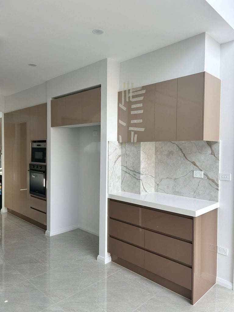 Modern kitchen with tan and brown cabinetry, marble backsplash, white countertops, and stainless steel appliances