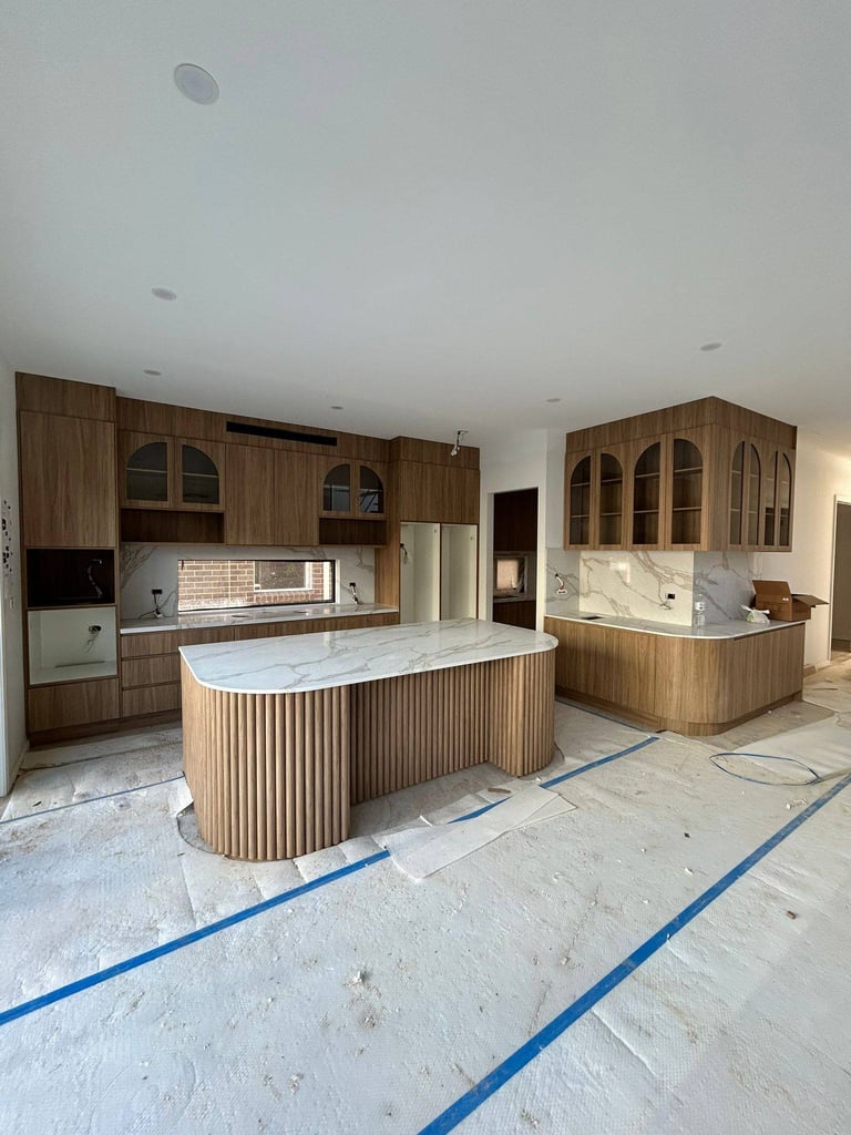 Modern kitchen under construction with wooden cabinetry, marble countertops, and stainless steel appliances.