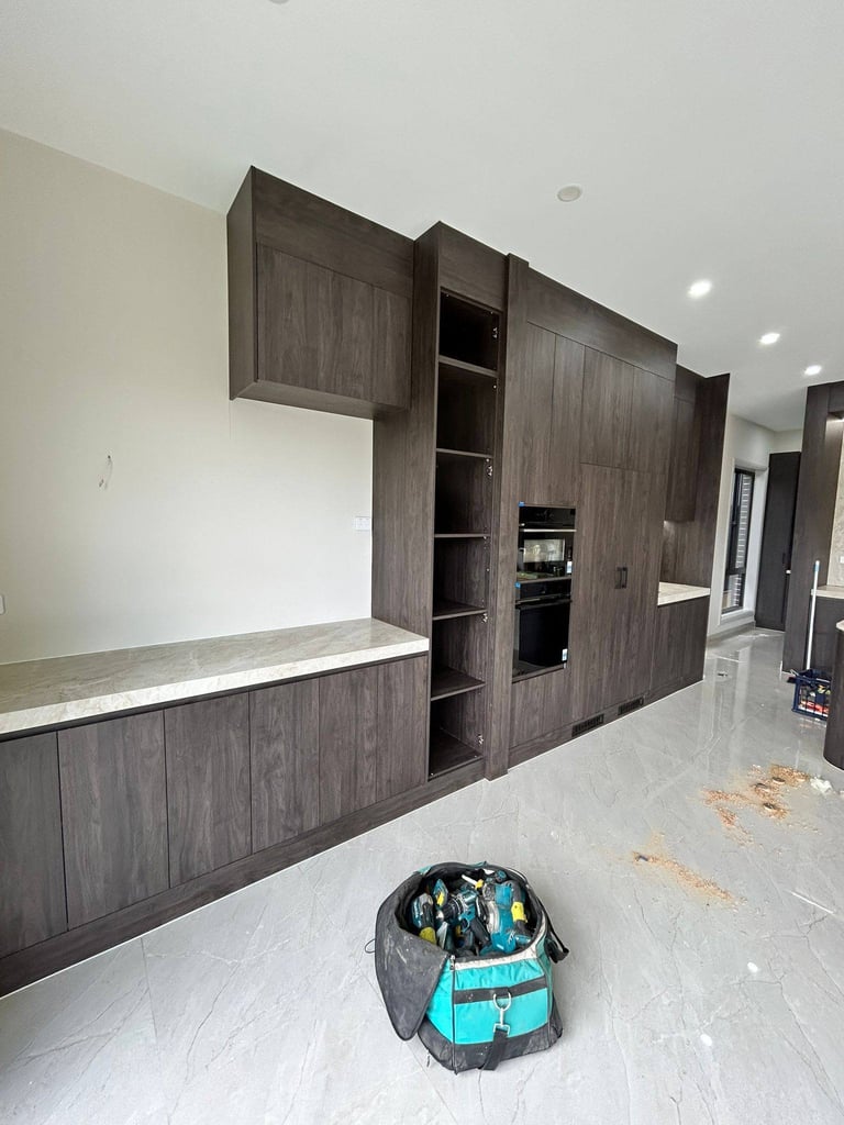 Modern kitchen with dark wood cabinetry, white countertops, and open shelving, with a blue backpack on the white floor