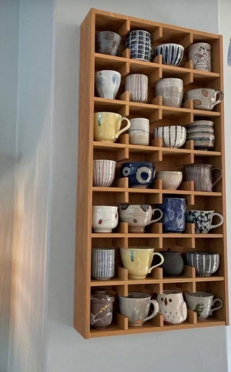 Wooden wall-mounted display shelf with multiple compartments holding a collection of decorative ceramic mugs and cups in various colors and patterns