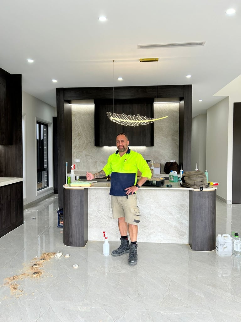 Man in neon yellow shirt standing at modern kitchen counter in open-concept home with marble flooring and recessed lighting