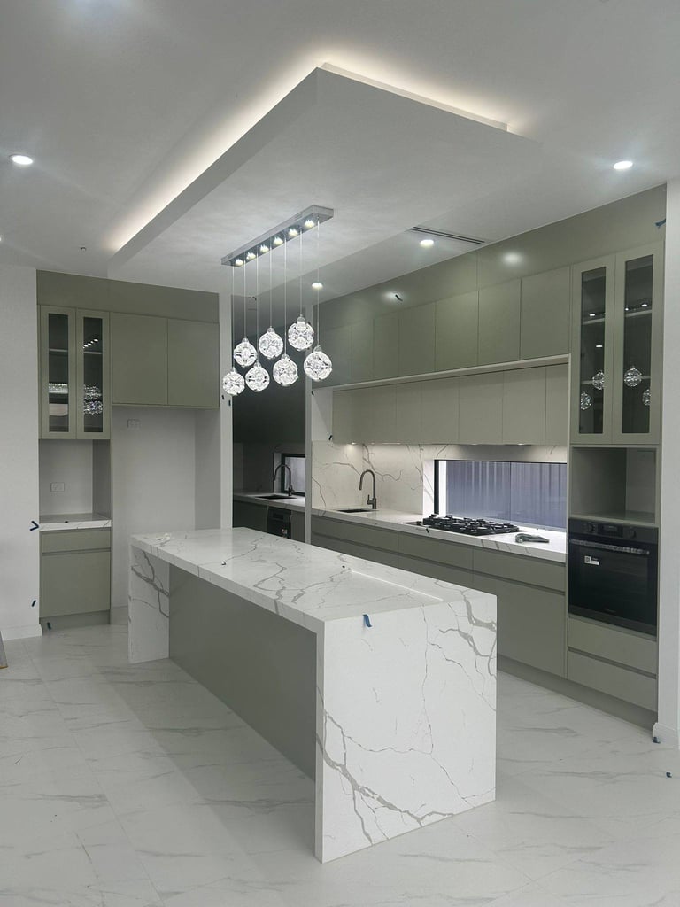 Modern kitchen with green cabinetry, white marble island, pendant lights, and sleek black appliances