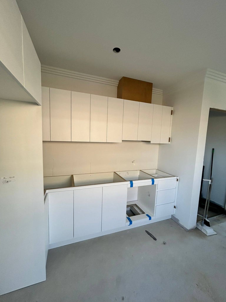 Unfinished kitchen with white cabinetry, exposed countertop, and concrete flooring during renovation