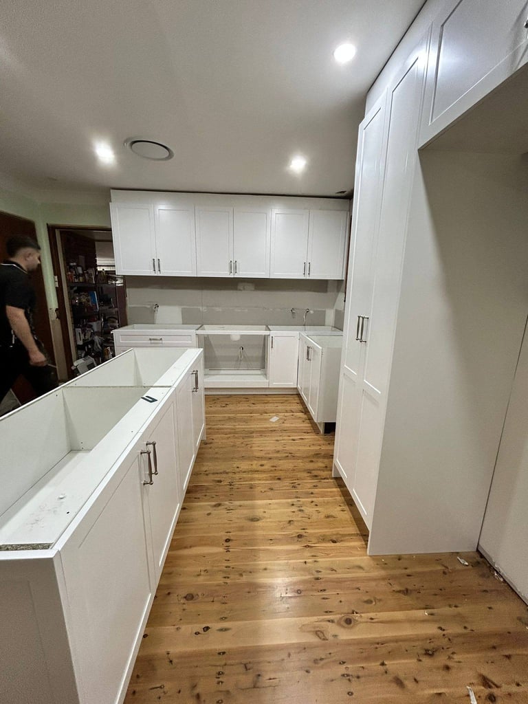 Modern kitchen with white cabinetry, wooden flooring, and stainless steel appliances under construction