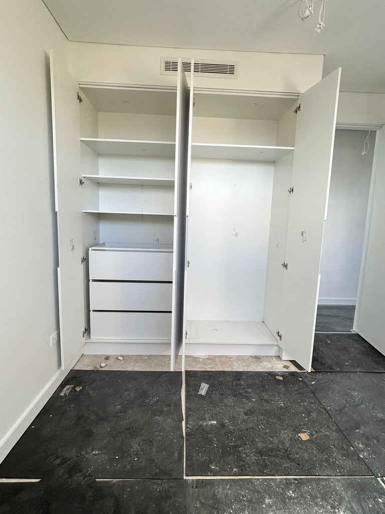 Empty walk-in closet with open white doors showing shelves and drawers on dark flooring