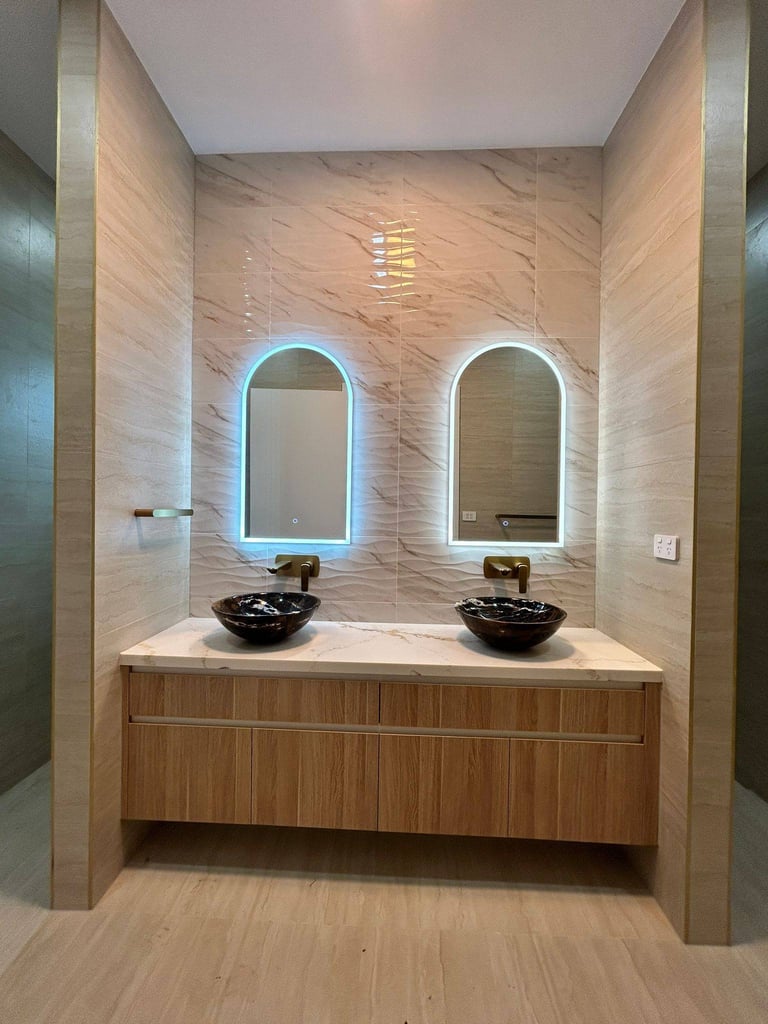 Modern double sink bathroom vanity with neon-lit arch mirrors, black vessel sinks, and beige marble tile walls