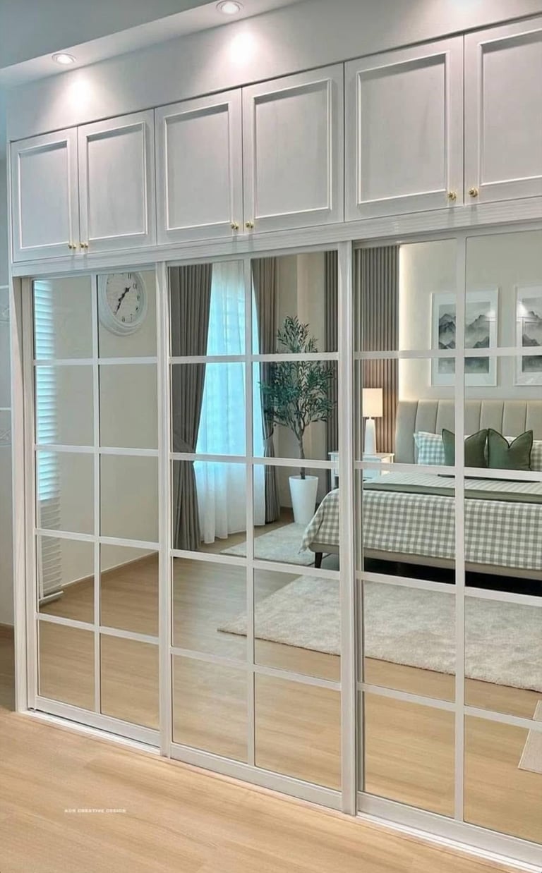 White mirrored wardrobe with glass doors and panels reflecting a modern bedroom interior with bed and natural light