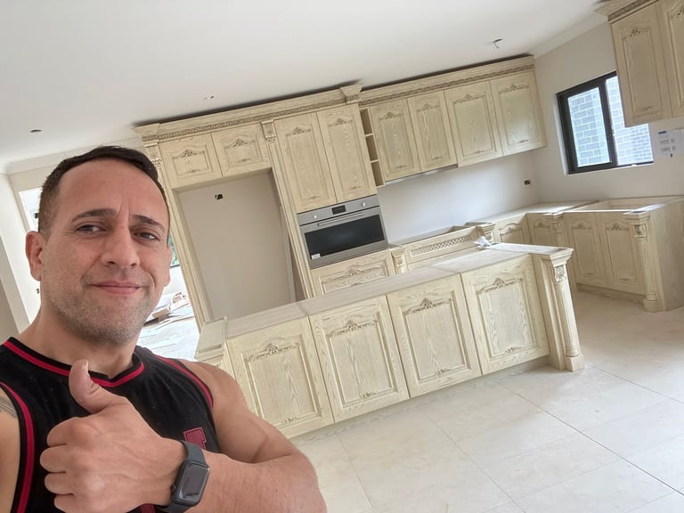Man giving thumbs up in front of empty cream-colored kitchen with white tile flooring and built-in appliances