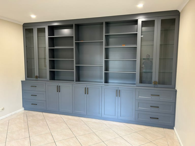 Built-in gray cabinetry with glass-door upper shelves and lower storage drawers in an empty room with tile flooring