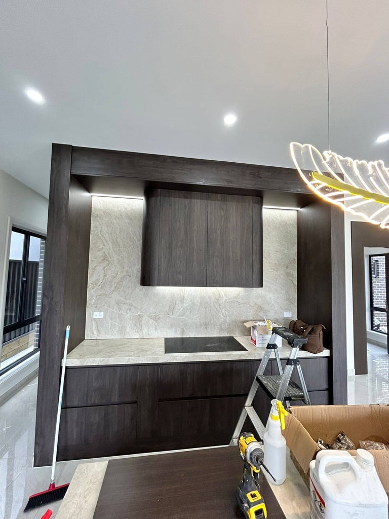 Modern kitchen showroom display with dark wood cabinetry, marble countertop, and minimalist design under recessed lighting