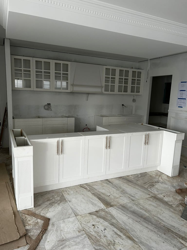 White kitchen cabinetry and countertops under construction in an empty room with tile flooring